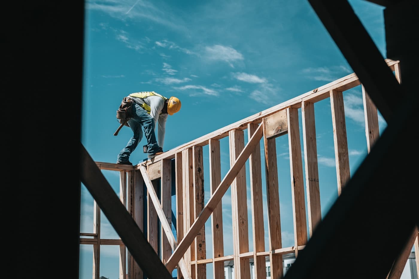 Bouwvakker met helm aan het werk op een houten skeletbouw tegen een blauwe lucht