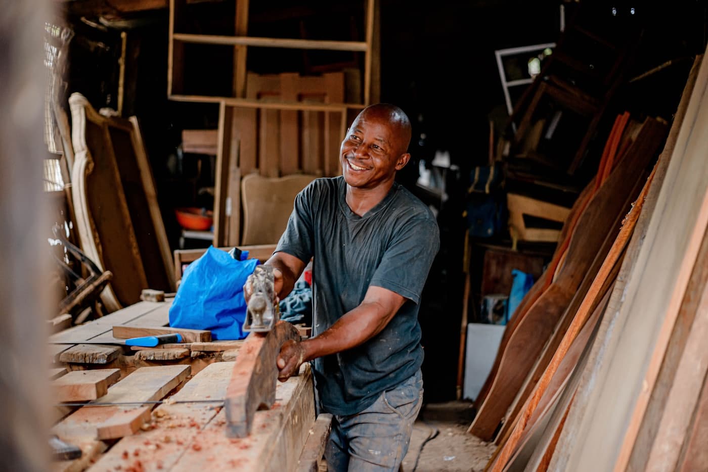 Timmerman schaaft lachend een plank hout in een volle werkplaats
